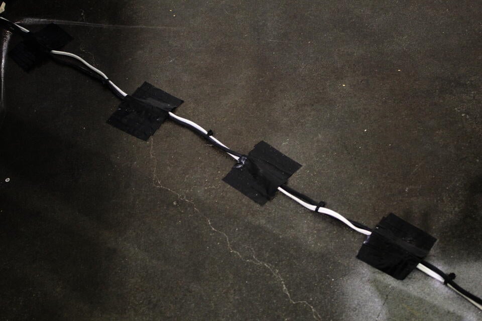 One black wire and one white wire are taped deliberately along the floor with black electrical tape.