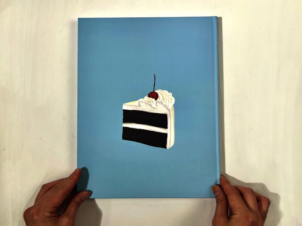 A photograph of the book cover, which features a piece of creamy white cake with a cherry on top, sitting on a baby-blue background