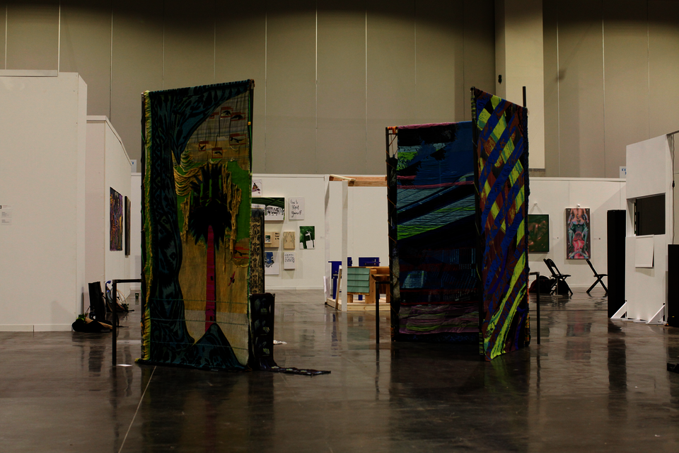 Large scale installation of metal steel frames with colorfull weavings standing in the middle of the floor at the convention center.
