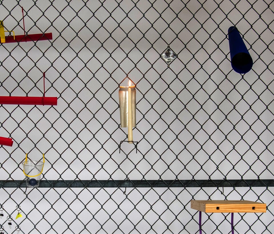 Close up of a chain link fence with various designed objects affixed to it, including a candle holder and a blue telescope.