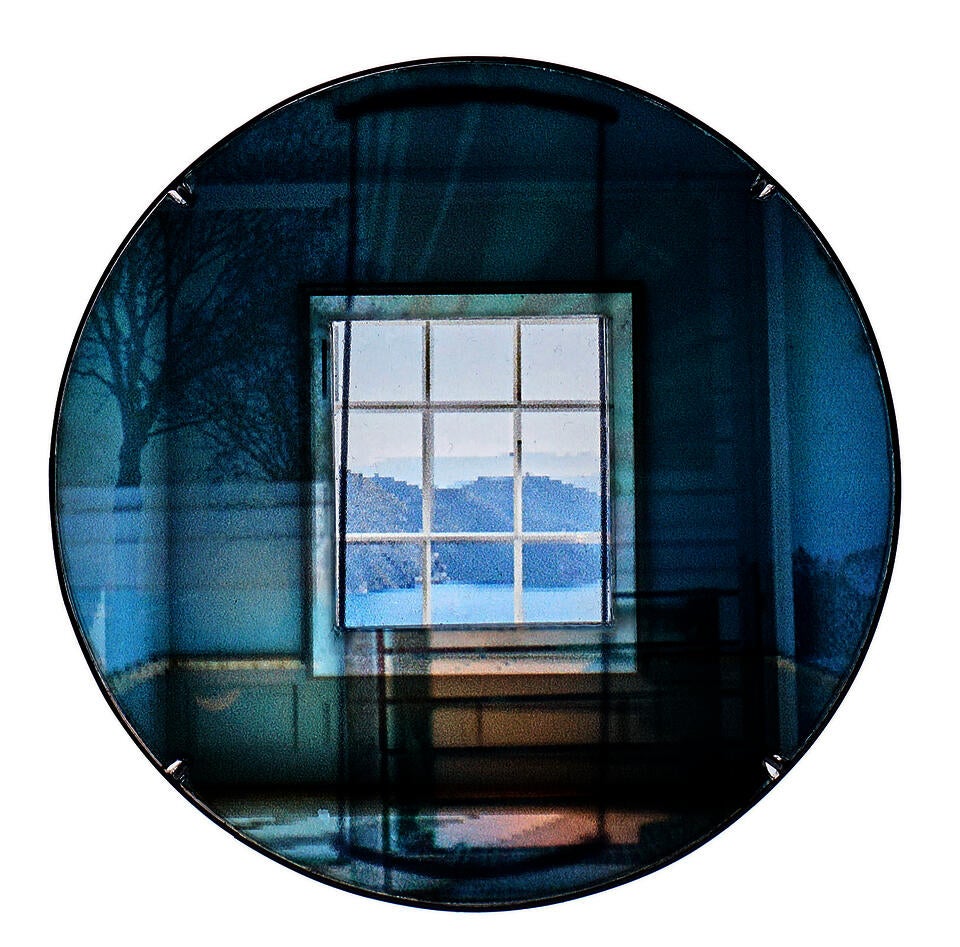 Blue circular brooch showing a square window view, with layered tree shadows and abstract light blending in a dreamlike room.