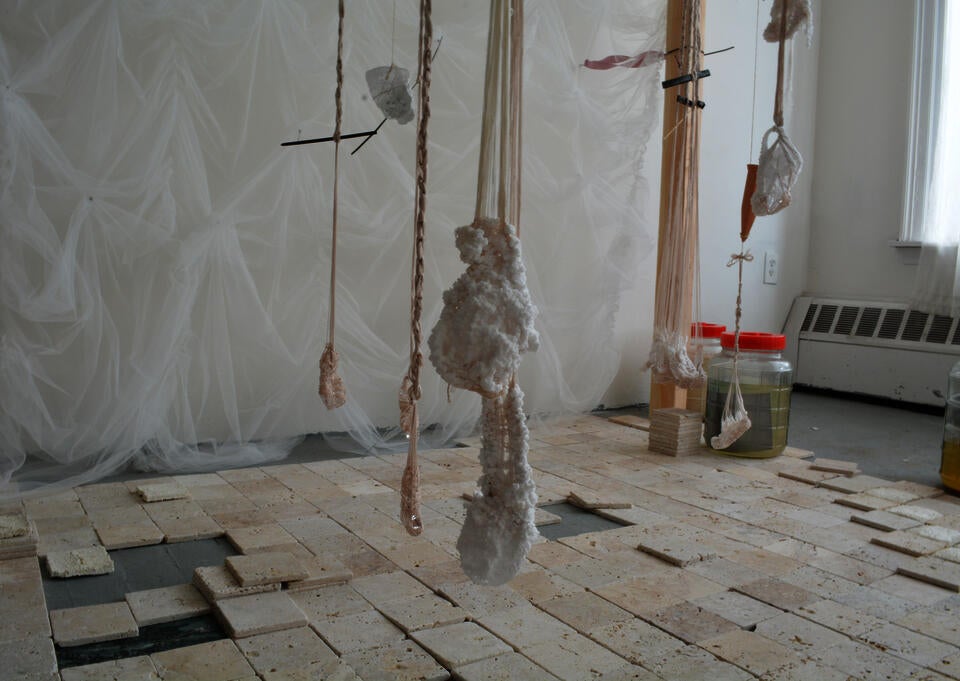 An installation of travertine tiles below threads that wrap around pieces of glass and coated in salt.