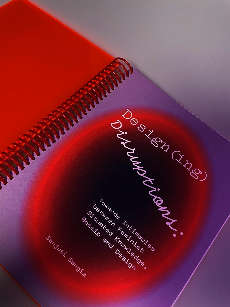 A lilac and orange cover of a spiral-bound book titled Design(ing) Disruptions by Senjuti Sangia. 