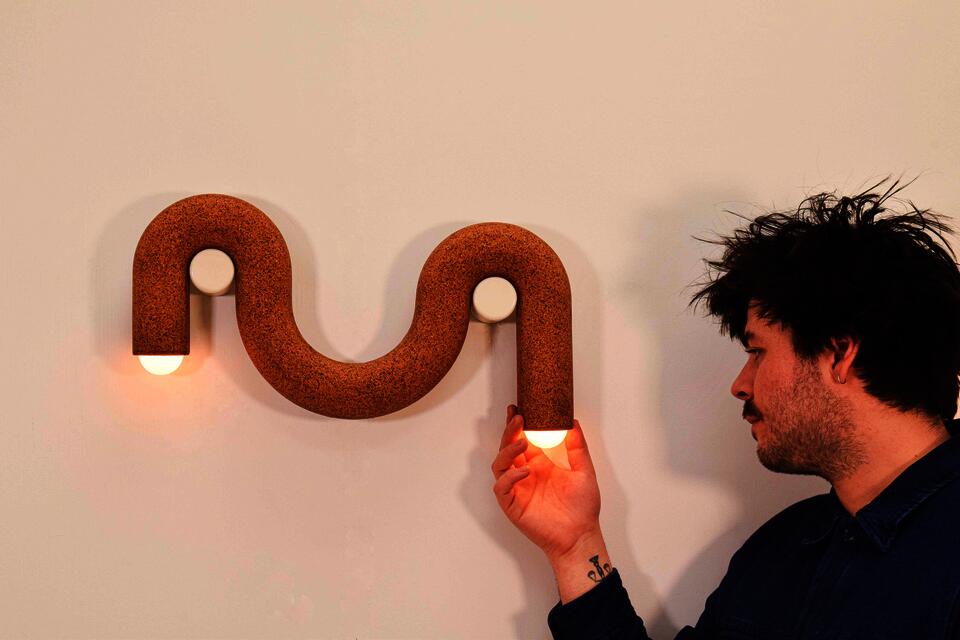 A brown cork cylinder droops over two white pegs like a noodle; bulbs protrude from both ends.