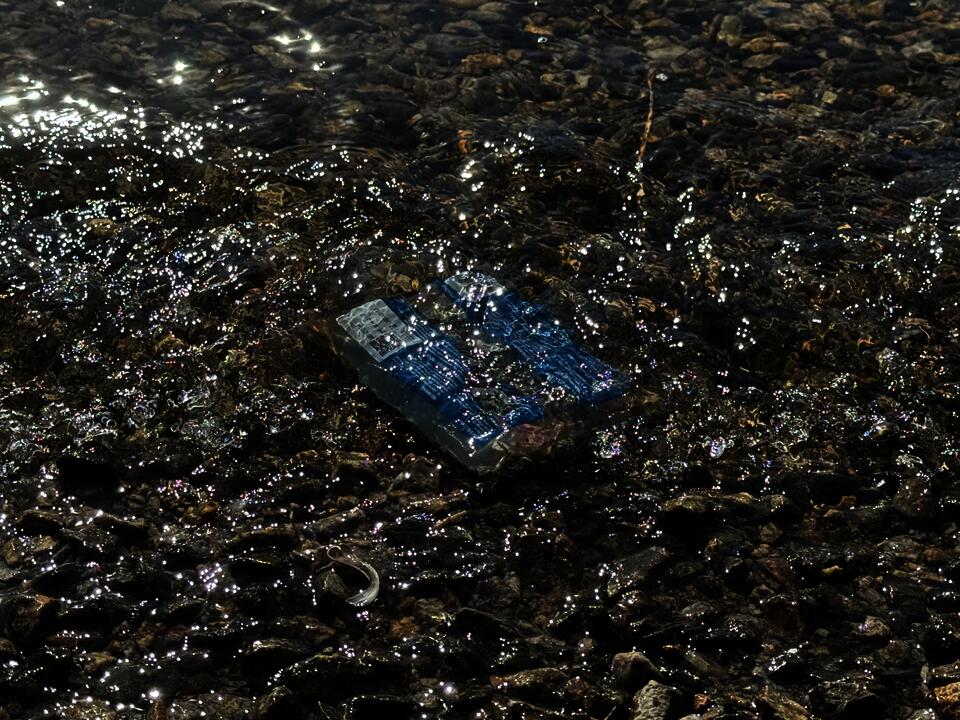 A blue plastic bag floating in shallow river water, surrounded by rocks and shimmering sunlight.