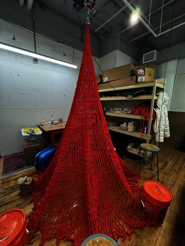 Red net hanged with ceramic objects dangled from a hoist. Hoist perform motion of let net spread on floor and pull it back up