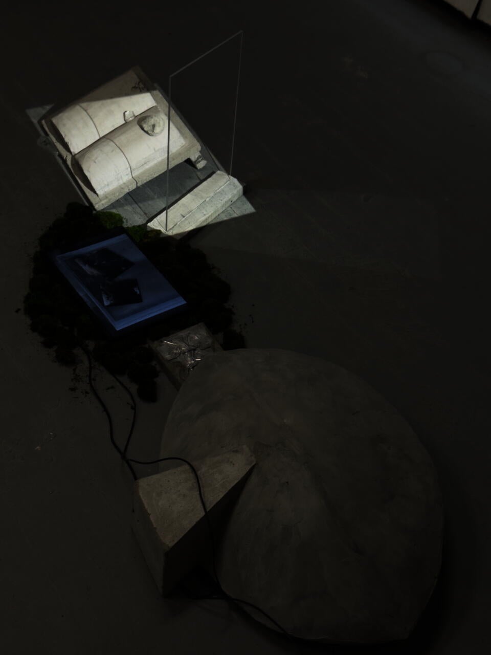 Concrete dome, moss-framed screen with floating mirrors, and book-like slab lit by dripping water’s shadow through glass.