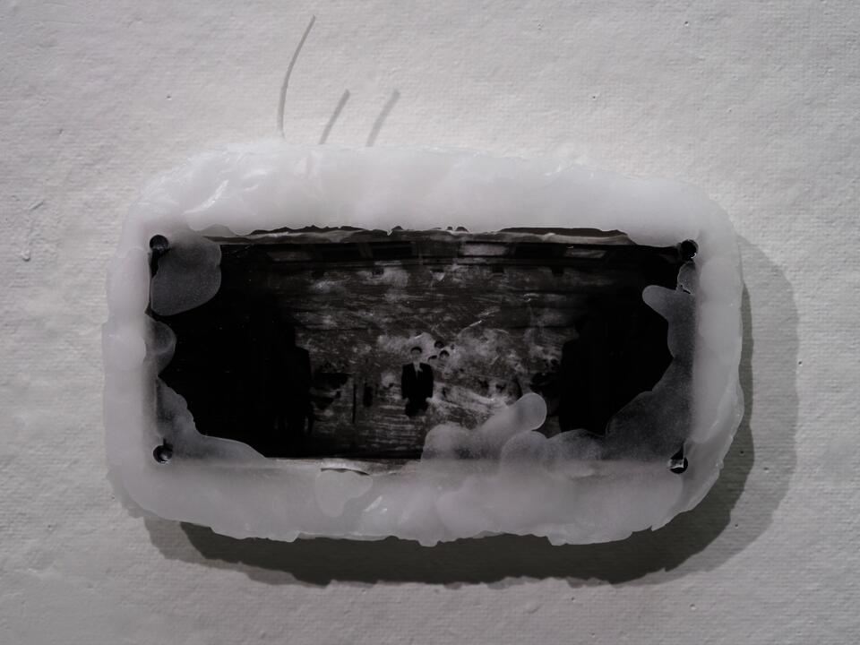 Close-up of a black-and-white family photograph partially covered in white paraffin and mounted on a wall.