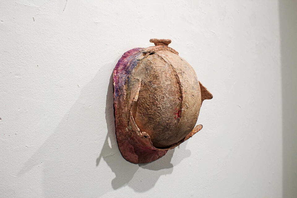 A construction worker's helmet covered by a crusty pink material. Hung flat on the wall.