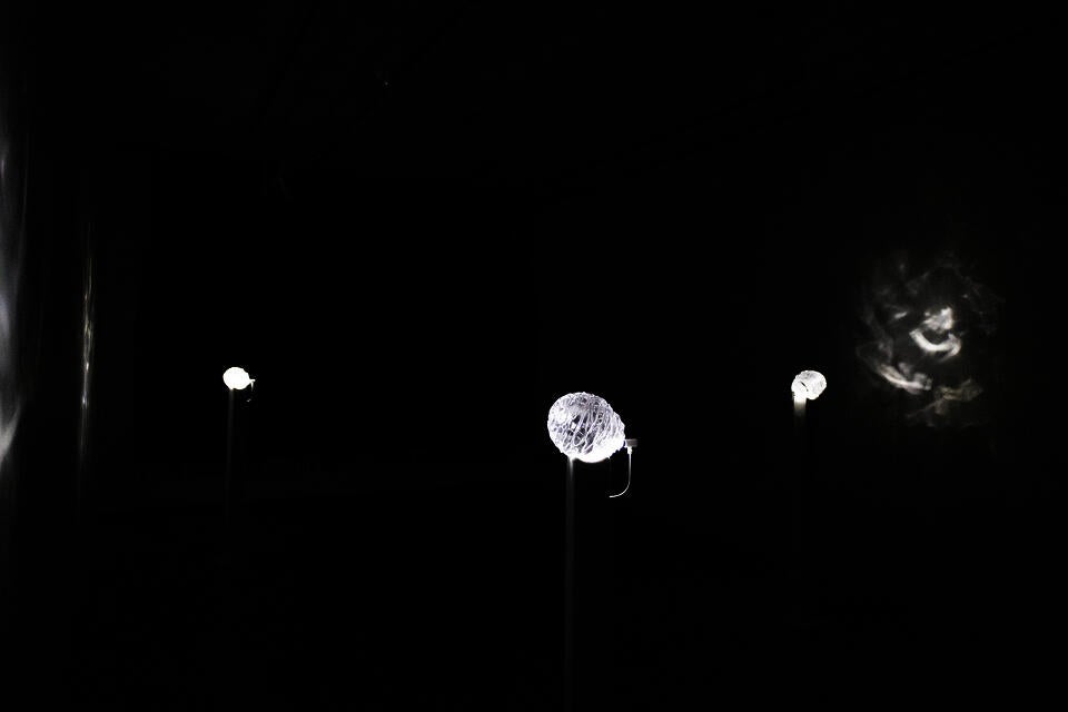 A dark room with three glass orbs on tall, thin pedestals. A small light shines on each orb, causing the orbs to glow and cast caustic light effects onto the walls nearby. 