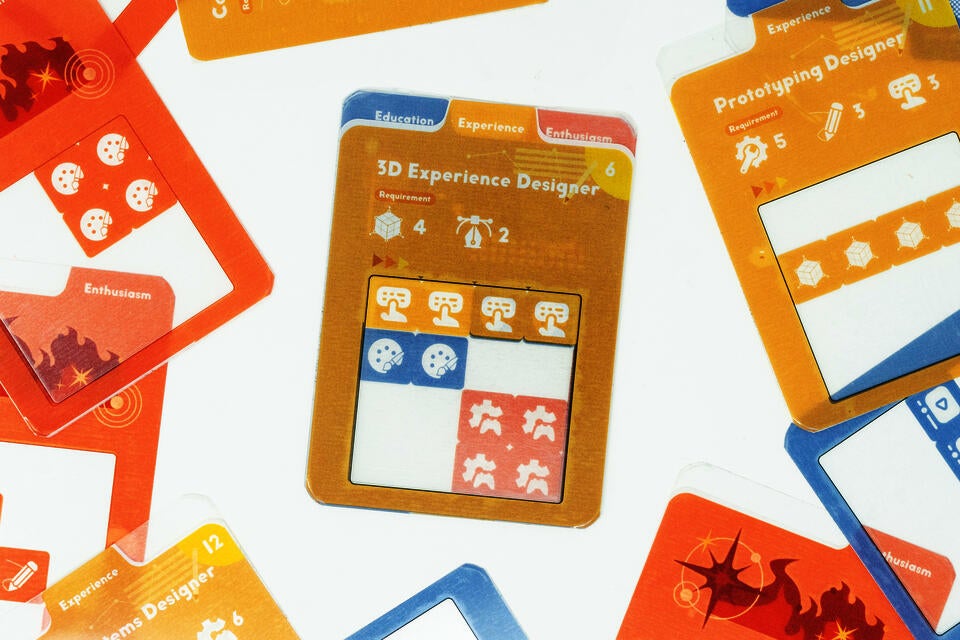 Colorful tabletop board game prototype showing transparent overlay cards, modular experience tiles, and job-description cards used for resume-building and persuasive communication role-play.