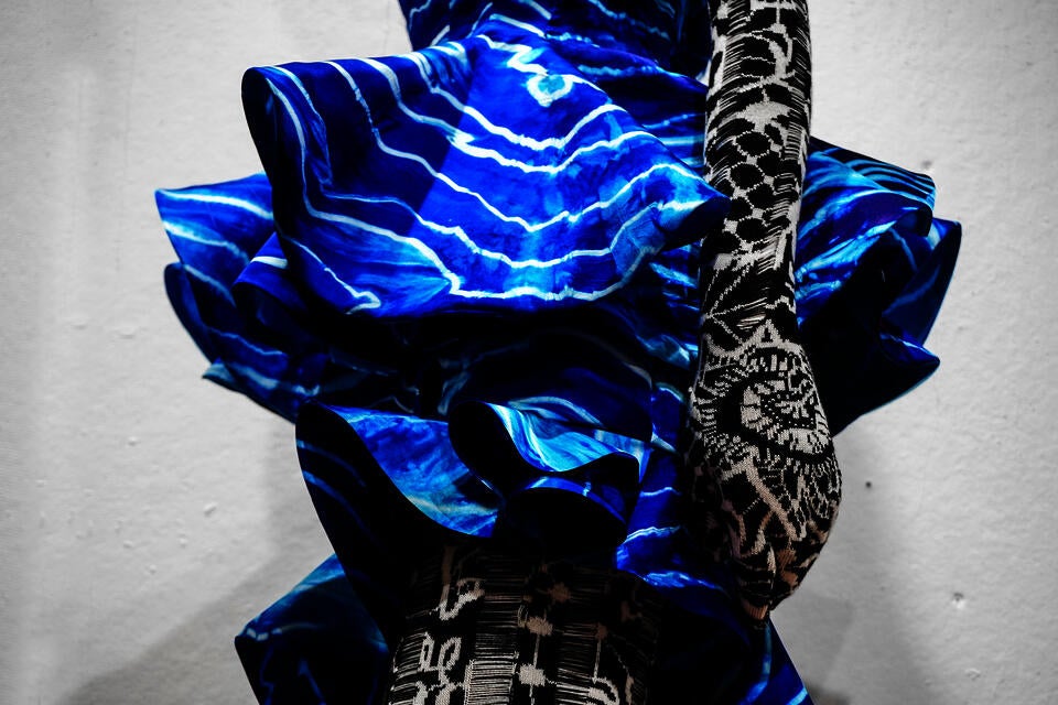 Close-up of sculptural blue silk ruffles with wave-like tie-dye patterns over black-and-white jacquard knit