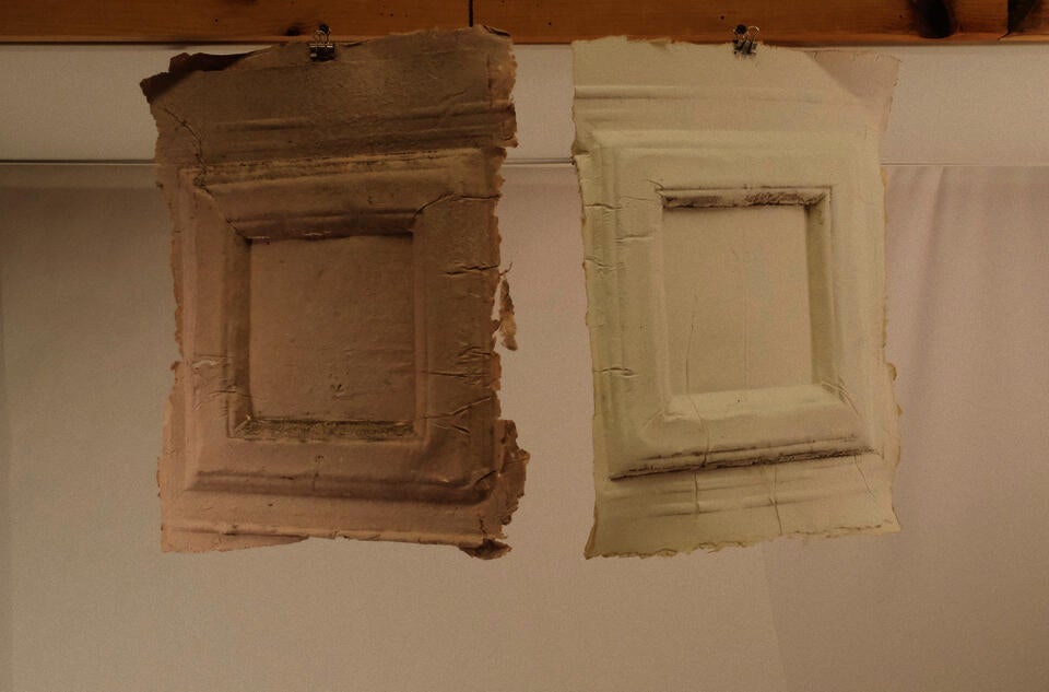 " Two completed paper casts from the vestibule of the Kendrick-Prentice-Tirocchi House, photographed in the studio after drying and removal from the wall. Each sheet carries the irreproducible impression of the surface it received — the ornament, the texture, the accumulated evidence of the space. Brought into the studio, the casts become both record and object, carrying the presence of the wall into a new context. Handmade paper, dimensions variable. 2026"