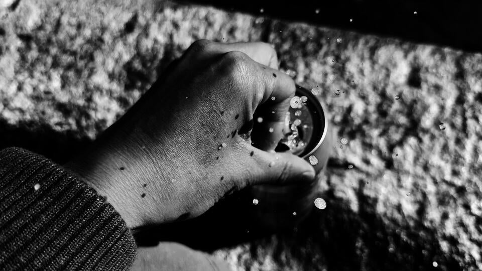 A black-white close-up photo of a hand opening a sparkling water with the liquid splashing out.